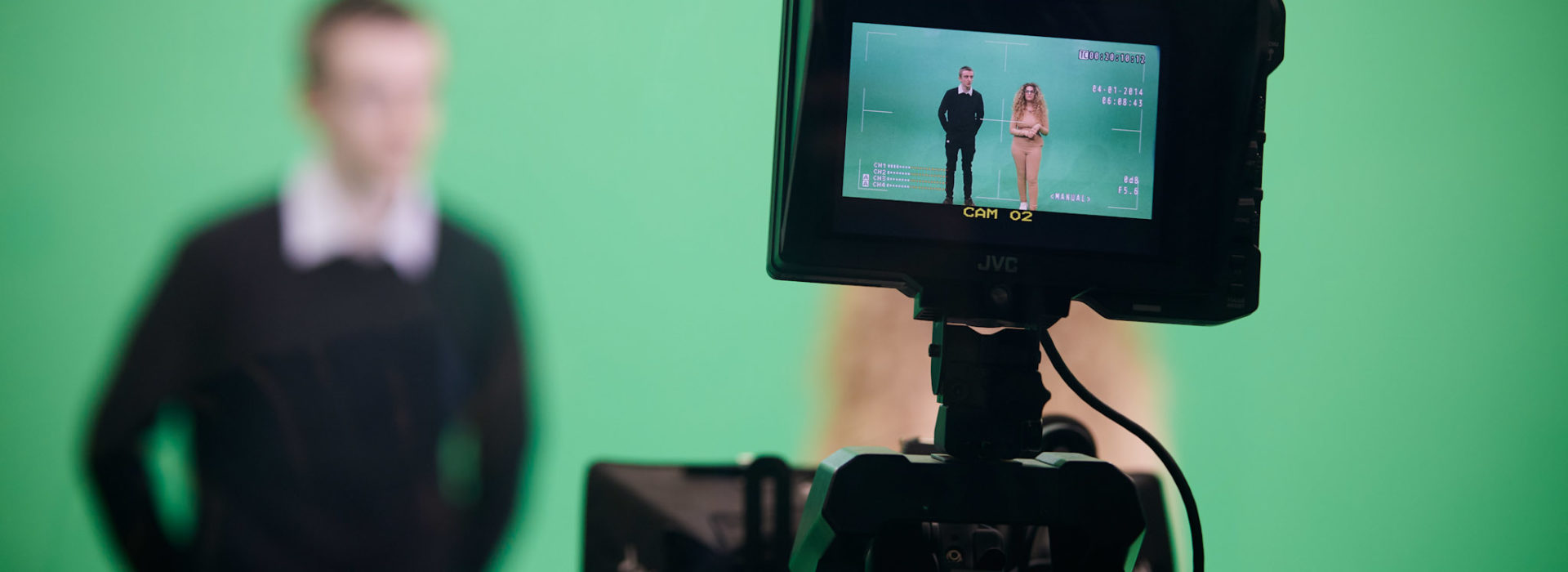 Two students in front of a green screen through a video camera