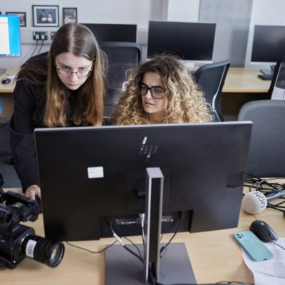 Two students in front of a green screen through a video camera