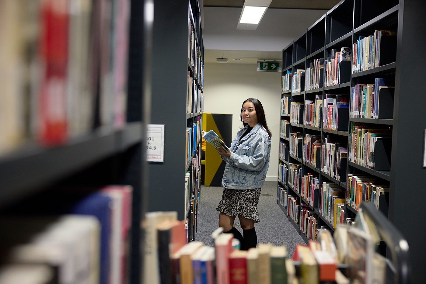 Student stands between two book stacks holding an open book