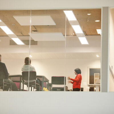 Students sat behind desks as a lecturer talks to them from the front of the classroom.