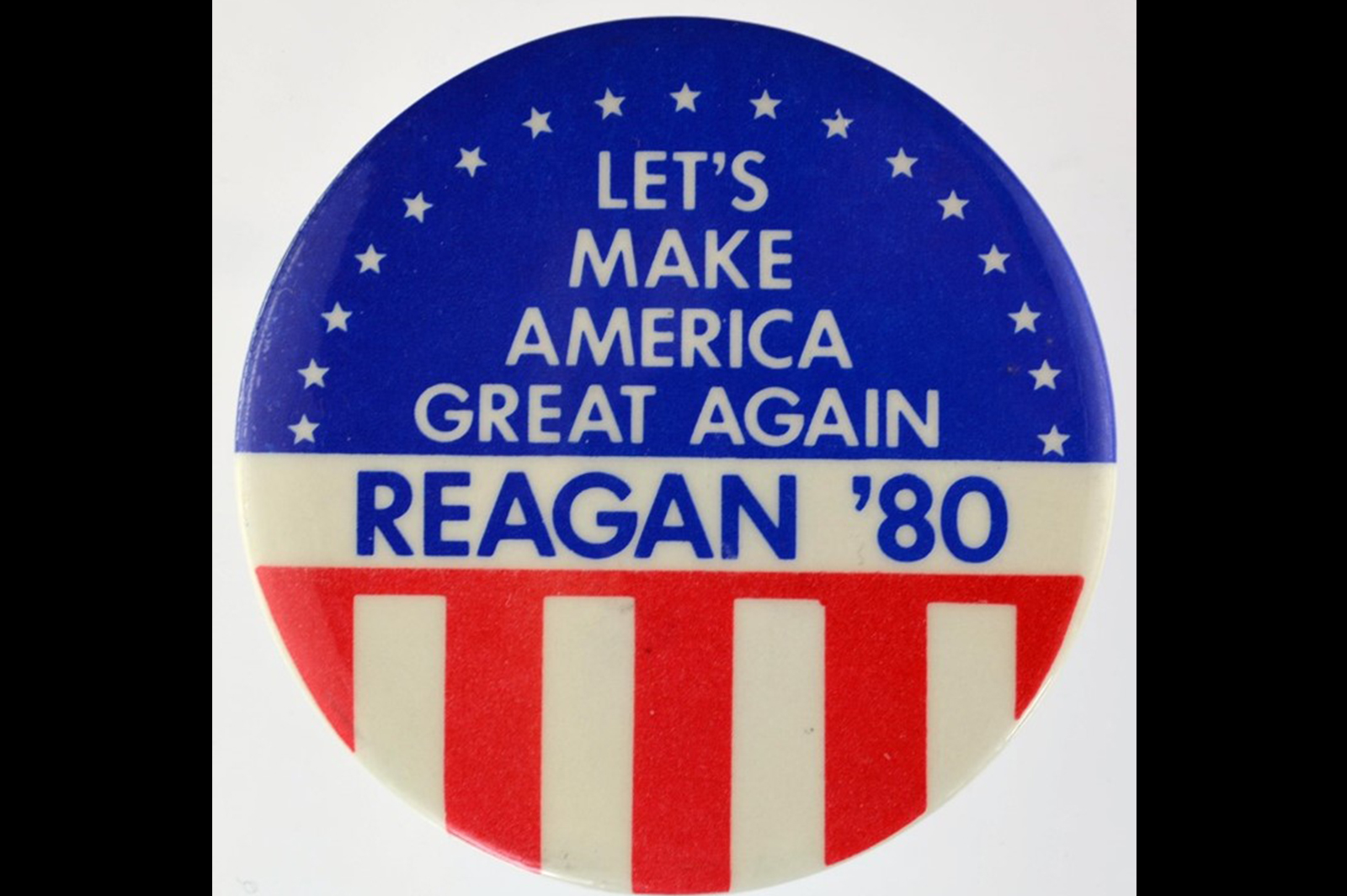 A red, white and blue coloured circular badge with the wording Let's Make America Great Again Reagan '80. The badge is decorated with stars and stripes