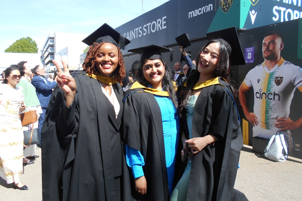Three students smile at camera in graduation gown and hat.