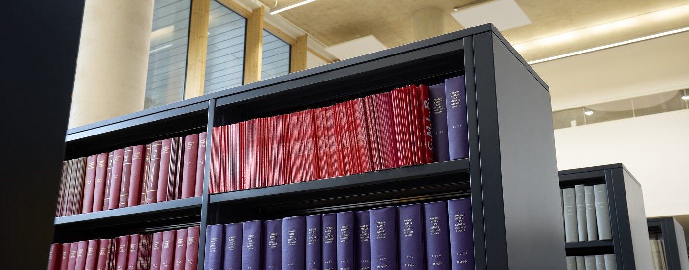 View of black bookshelves filled with neatly arranged books and journals, primarily with red and purple covers, under bright ceiling lights.