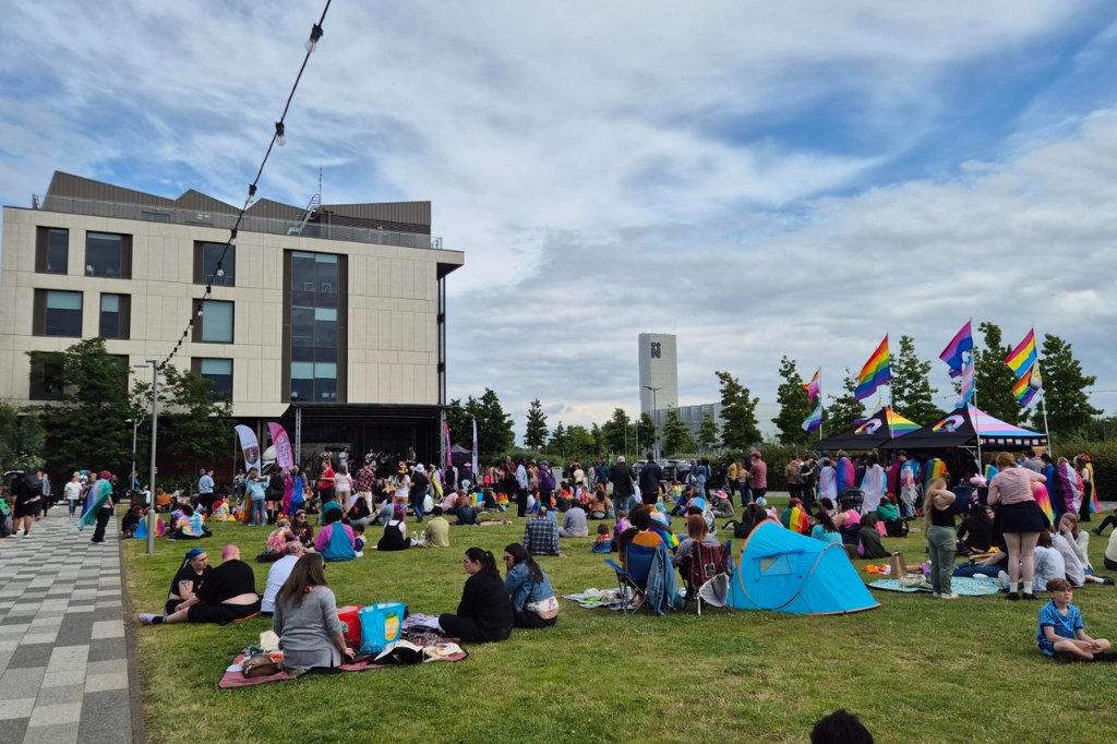 Crowd of people sit on lawn at Waterside Campus for Northampton Pride.