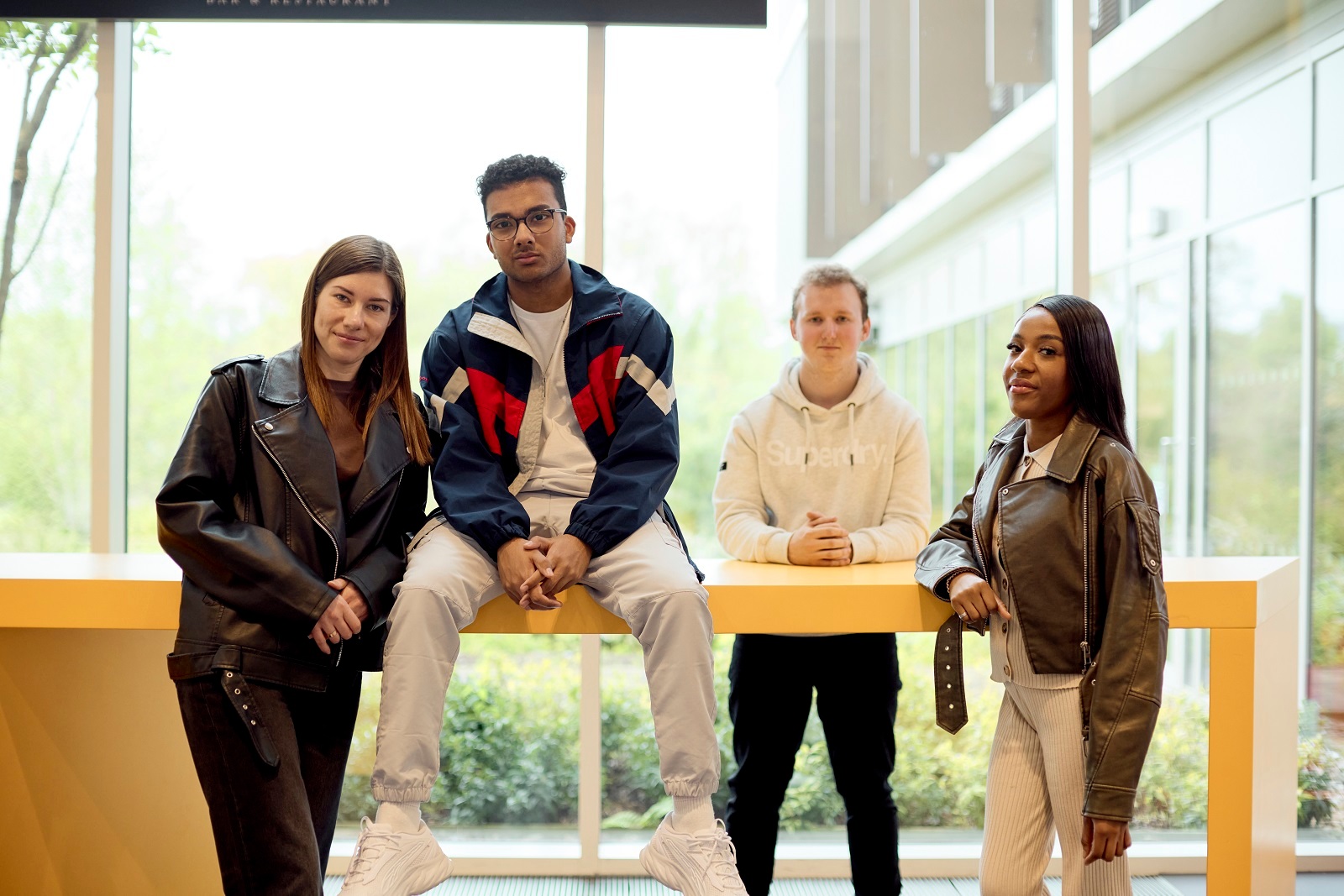 Four UON students stand and sit casually around a yellow table in the bright Learning Hub with large windows.