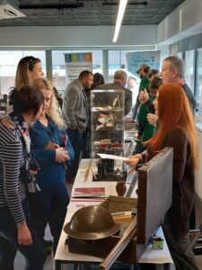 Visitors gather around a table with historic artifacts on display at the Heritage Education Fair. Some converse, while others examine the items.