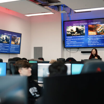 Overhead view of five students sitting around a white table in the Learning Hub. Each is working on a laptop. The floor-to-ceiling windows by the table overlook a lawn.