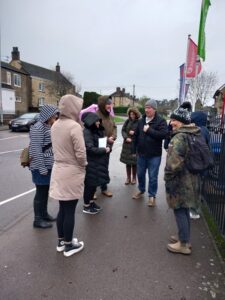 A group of people on a heritage trail in Corby old Village. They are standing on a street corner wearing winter outdoor clothing, including coats and hats.