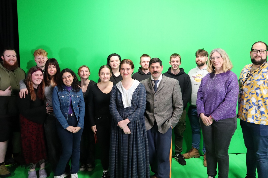 Group photo of students and staff in front of green screen.