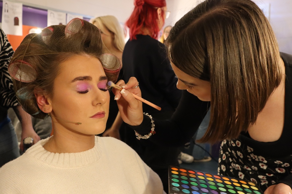 Student applies makeup to actress using a brush.