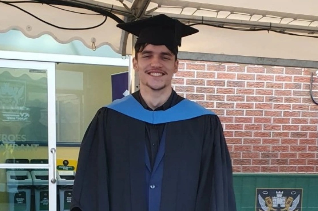 Jordan Tomkins smiles at camera in graduate hat and gown.