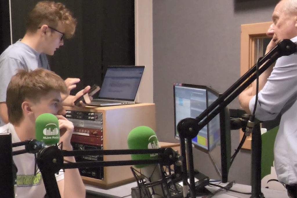 Students speak into mic and work on computers at election coverage radio studio.