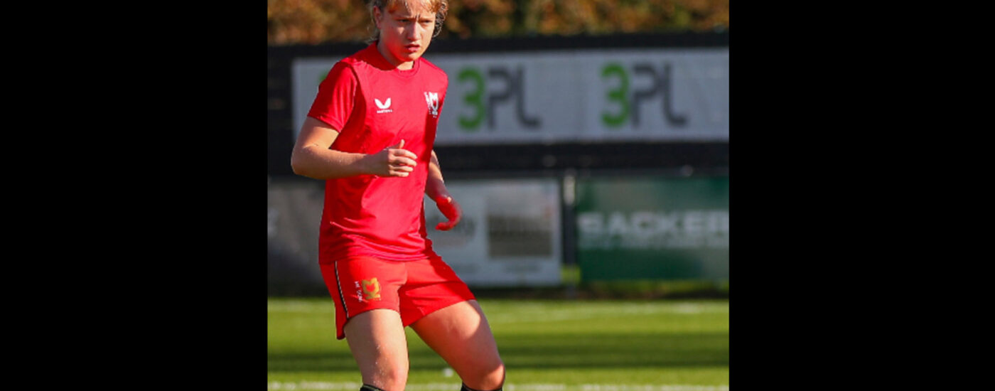 Chloe Martin wearing a red MK Dons football kit while playing a game.