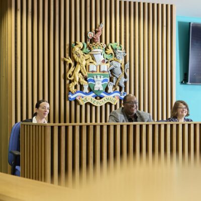 Students sat behind desks as a lecturer talks to them from the front of the classroom.