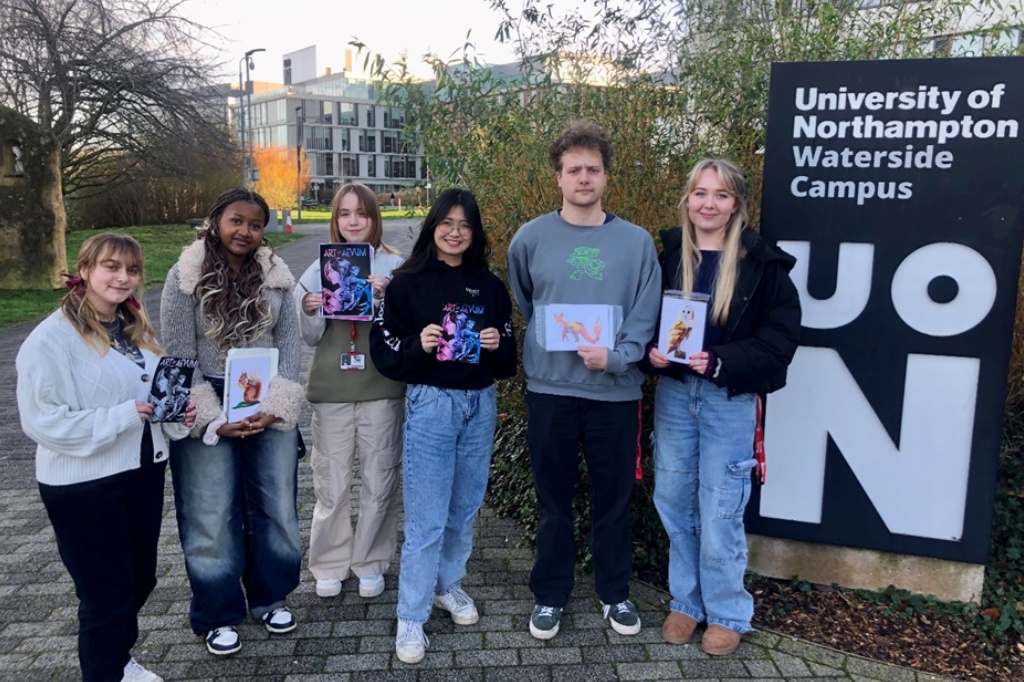 Group photo of students holding up booklet next to UON sign.