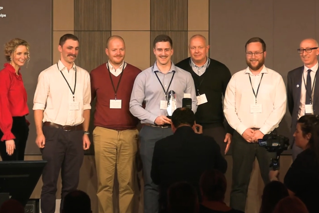 Five members of UON and SLG hold award on stage and smile at camera.