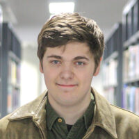 Joe Glover, standing in between two bookshelves looking at the camera and smiling.